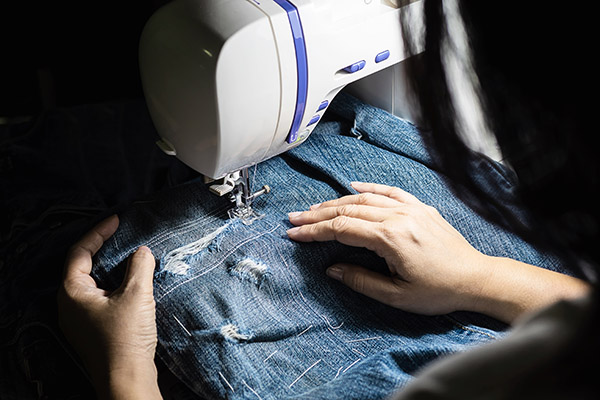Woman doing jeans patchwork using sewing machine - home DIY sewing concept